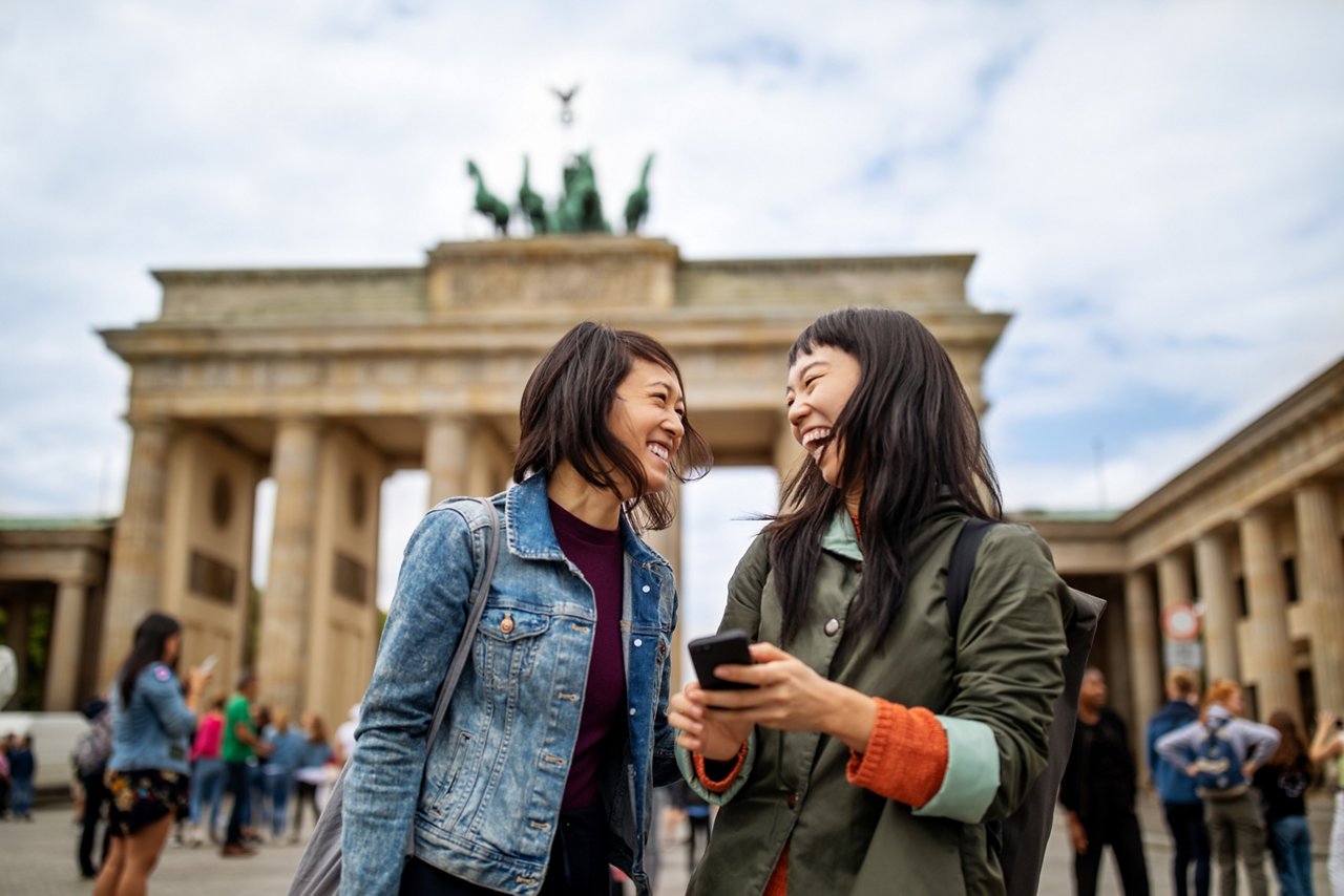 Cheerful female friends standing against Brandenburg Gate in city during vacation