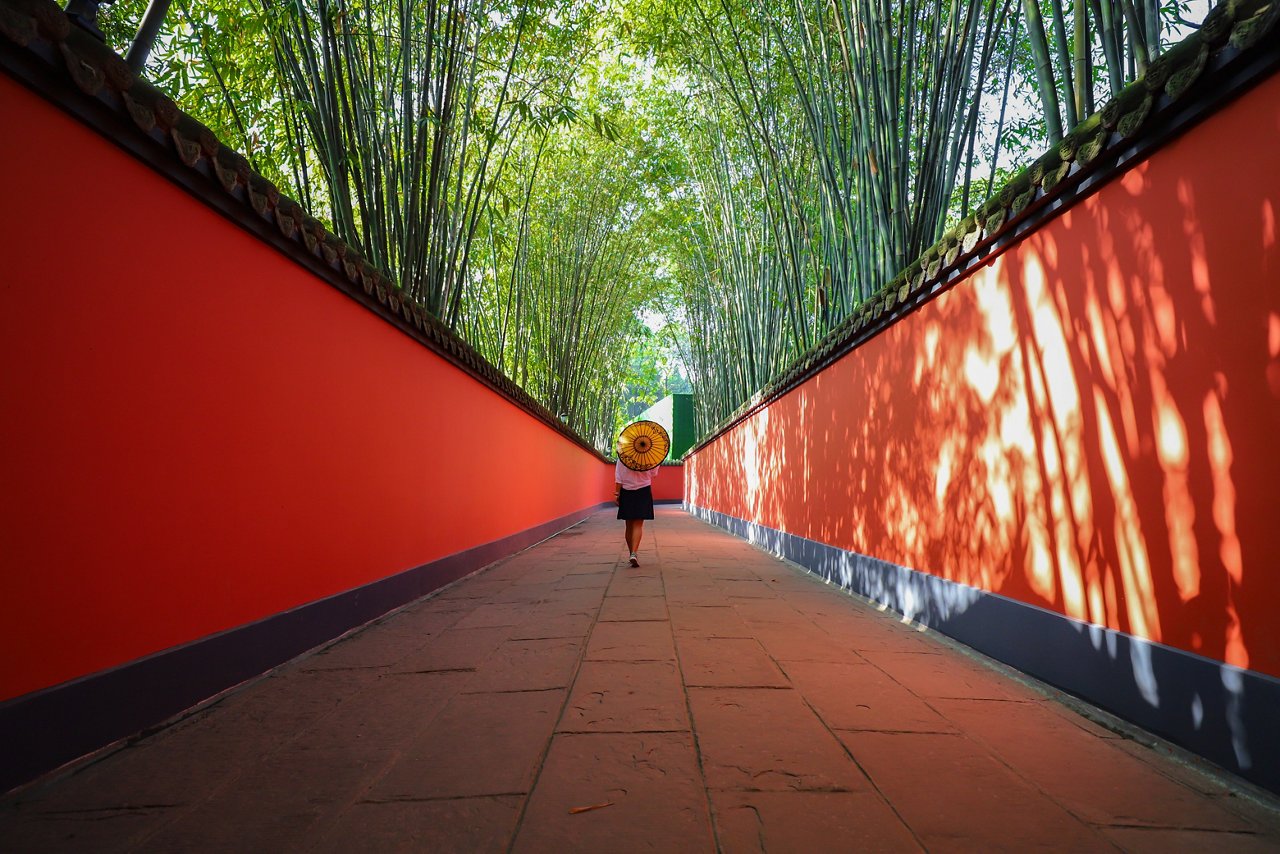 A woman from behind walking with an umbrella along the curvy red wall passage of Wuhou Temple at Chengdu, Sichuan Province, China.